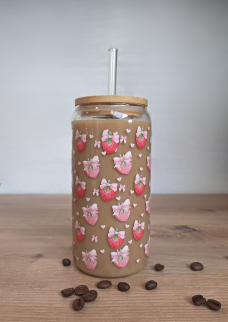 Glas mit buntem Erdbeer-Muster, gefüllt mit einem Kaffee-Getränk und einem Strohhalm.